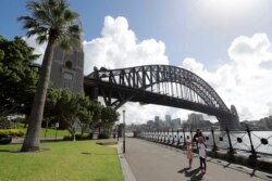 Seorang perempuan dan dua anak berjalan di bawah Harbour Bridge, Sydney, Australia, Selasa, 6 April 2021.