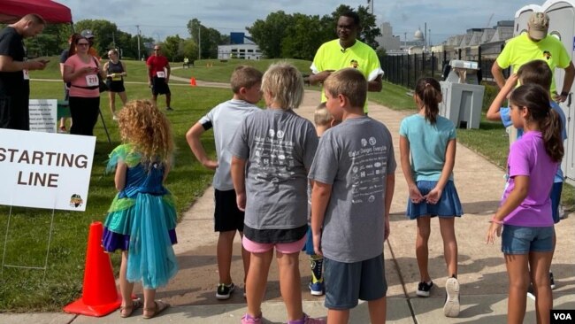 Representative Samba Baldeh, in bright green at center, greets young runners in a fundraiser for nonprofit Strides for Africa, an event during Africa Fest 2021 in Madison, Wis. Aug. 21, 2021. (Carol Guensburg/VOA)