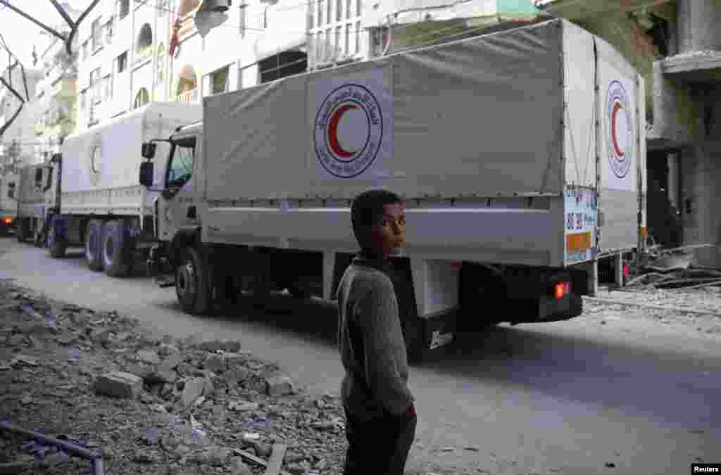 A boy stands as an aid convoy of Syrian Arab Red Crescent drives through the besieged town of Douma, Eastern Ghouta, Damascus.