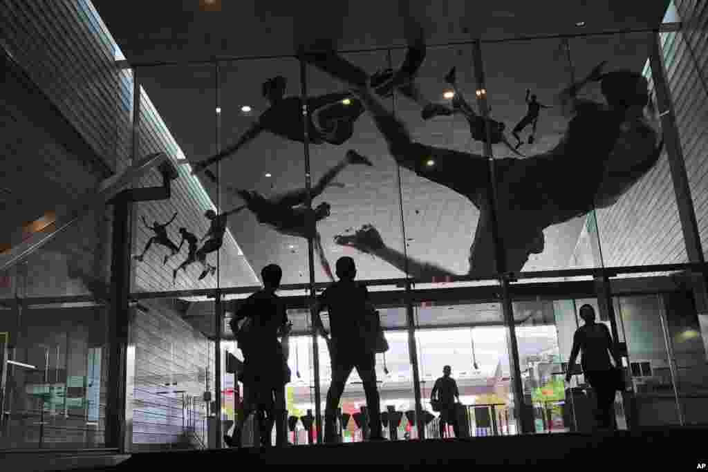 People look at&nbsp; the glass entrance of a subway station in Singapore which is decorated with decals of athletes in action.