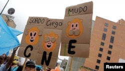 Opposition supporters hold placards during a rally to demand a referendum to remove President Nicolas Maduro in Caracas, Venezuela, May 14, 2016. From left, the placards read "Deaf," "Blind" and "Dumb." "CNE" on the placards refers to the National Electoral Council.