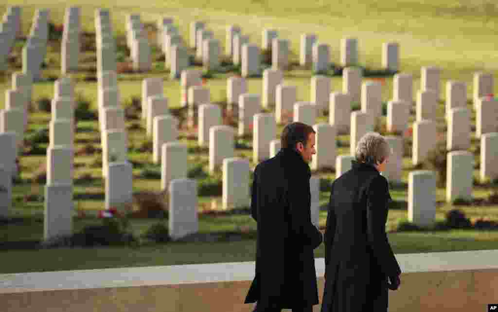 British Prime Minister Theresa May, right, and French President Emmanuel Macron walk together past gravestones after laying wreaths at the World War I Thiepval Memorial in Thiepval, France,.