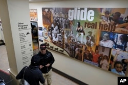 In this Feb. 12, 2019 photo, people walk past a display and directory to the many assistance programs at the Glide Memorial United Methodist Church in San Francisco.