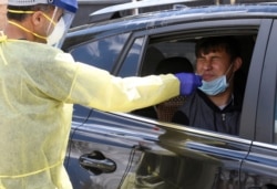 In this April 22, 2020 photo, Ganga Khadka, a refugee from Nepal, gets a test for the coronavirus in the parking lot of Dr. P.J. Parmar's clinic in Aurora, Colo.