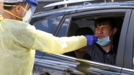 In this April 22, 2020 photo, Ganga Khadka, a refugee from Nepal, gets a test for the coronavirus in the parking lot of Dr. P.J. Parmar's clinic in Aurora, Colo.