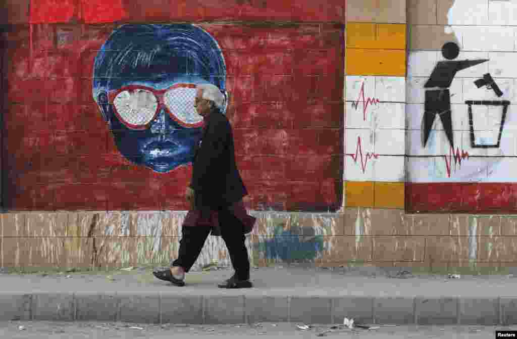 A man walks past a wall adorned with graffiti painted by various artists to promote peace, along a sidewalk in Karachi, Pakistan.
