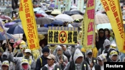 Demonstrators in raincoats and umbrellas march with banners and placards during an anti-nuclear protest on a street, amid rainfall in Taipei, March 8, 2014.
