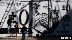 People stand in front of graffiti mocking the Brazilian currency note, the real, in downtown Rio de Janeiro, Brazil July 31, 2014. 