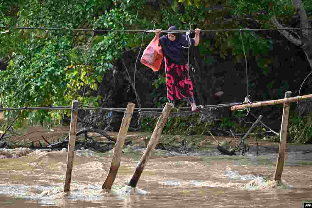 A woman crosses a river using the remains of a bridge, swept away during last year&#39;s flooding, at Malela village in Luwu Regency, South Sulawesi, Indonesia.