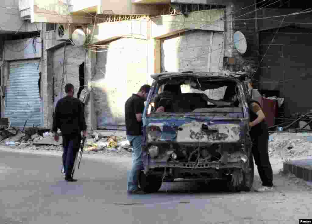 Men check a damaged vehicle as a Free Syrian Army fighter, carrying his weapon, walks by in the besieged area of Homs, Syria, May 27, 2013. 