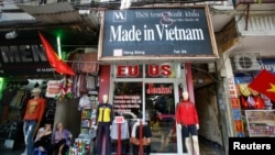 FILE - Vendors sit outside a shop selling clothes in Hanoi, Oct. 3, 2014.