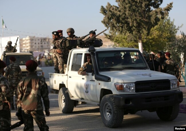 FILE - Fighters of National Army, backed by Turkey, stand at a back of a truck in the city of al-Bab, Syria, Aug. 5, 2018.