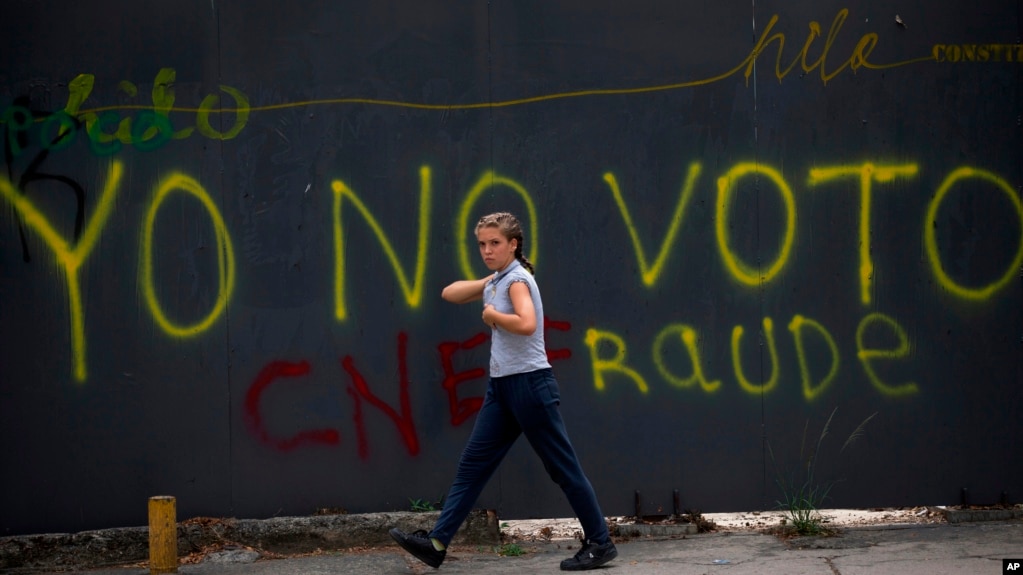 Una transeÃºnte pasa frente a un grafitti en Caracas que censura la elecciÃ³n presidencial del 20 de mayo, califcÃ¡ndola de fraude.