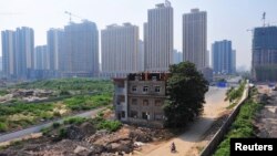 FILE - A man rides his bicycle past a partially demolished building in the middle of a street next to new residential construction sites in Xi'an, August 14, 2013. Some worry that, in pursuit of economic opportunities, Xi'an is trying to do too much too fast.