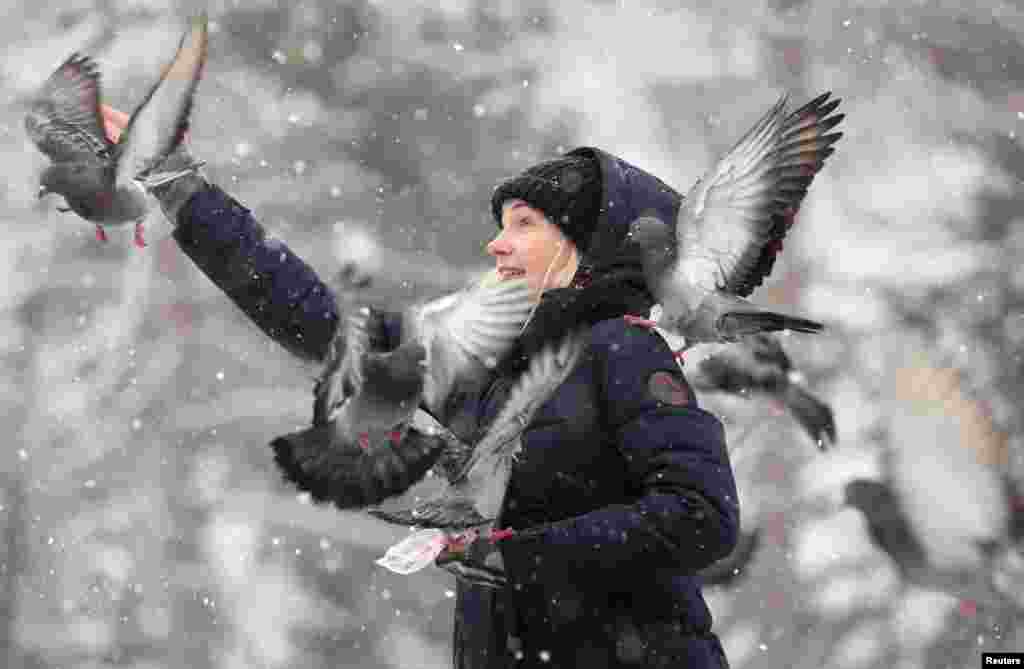 A woman feeds pigeons in a park during a snowfall in Almaty, Kazakhstan.