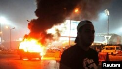 Một cổ động viên đứng gần chiếc xe cảnh sát bị cháy trong khi xô xát diễn ra giữa các cổ động viên và lực lượng an ninh trước sân vận động ở ngoại ô thủ đô Cairo, 8/2/15
