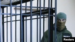 FILE - A member of the National Anti-Corruption Bureau of Ukraine stands guard next to a defendant's cage during a court hearing in Kyiv, Ukraine, April 21, 2017.
