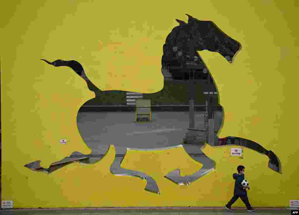 A boy walks in front of a horse sculpture in a park in Beijing.