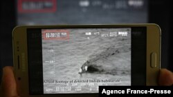 FILE - A Pakistani journalist watches a video released by Pakistan's Navy that allegedly shows an Indian submarine, on a smartphone in Islamabad, March 5, 2019.