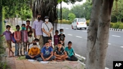 A former diplomat Virendra Gupta and his singer wife Veena Gupta pose for a photograph with underprivileged children whom they teach on a sidewalk in New Delhi, India, on Sept. 3, 2020. (AP Photo/Manish Swarup)