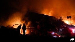 Two firefighters watch as a home burns in a wildfire in La Conchita, Calif., Dec. 7, 2017.