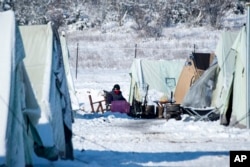 A migrant sits on a chair outside a tent at the snow-covered refugee camp in Vagiohori near the Greek city of Thessaloniki, Jan. 12, 2017.