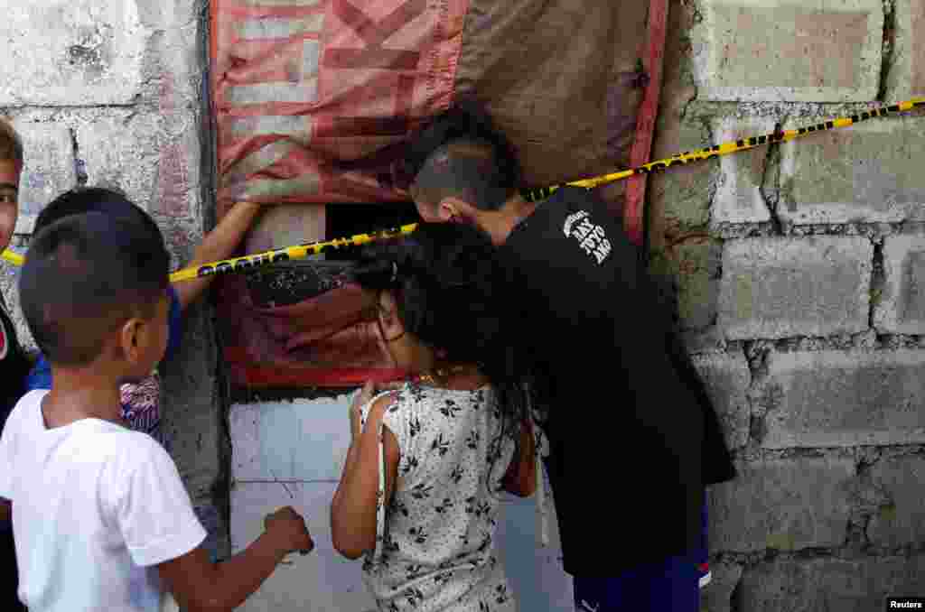 Anak-anak mengintip ke dalam ruangan di mana terdapat tujuh orang yang tertembak mati oleh yang dicurigai berada di rumah yang menurut keterangan polisi, menyimpan narkoba ilegal di Caloocan, Manila, Filipina.