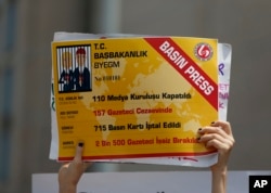 An activist holds a placard, made to look like a press card, that reads " 110 media organizations closed,157 journalists jailed, 715 press cards cancelled, 2.500 journalists fired " outside the court in Istanbul, July 28, 2017.