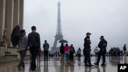 People walk past by French police officers, as they patrol at Trocadero plaza with the Eiffel Tower in the background in Paris, France, Saturday, May 6, 2017.
