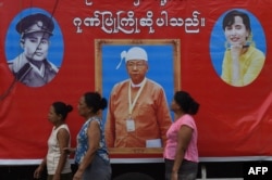 Relatives and sympathisers of political prisoners wait outside Insein prison in Yangon on April 8, 2016 in front of a banner bearing the portrait of new Myanmar President Htin Kyaw (C) democracy icon Aung San Suu Kyi (R) and the late Myanmar hero General Aung San (L), the father of Aung San Suu Kyi.