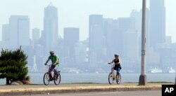 FILE - Cyclists pedal in view of downtown Seattle, cloaked in a haze of smoke from fires raging in British Columbia that swept down into the Puget Sound region, Aug. 3, 2017. Seattle, like many cities in the Northwest, has been plagued by hazardous smoke from wildfires.