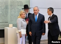 Israeli Prime Minister Benjamin Netanyahu, from left, and his wife Sara, alongside Agustin Zba, President of the Argentine Israeli Mutual Association Jewish community center, walk past a wall with names of the victims of the 1994 AMIA bombing in Buenos Aires.