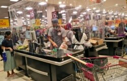 Cashiers serve customers from behind a plastic sheet barriers installed as a precaution against the new coronavirus outbreak, at the supermarket at AEON shopping mall in Tangerang, on the outskirts of Jakarta, Indonesia, Friday, May 22, 2020.