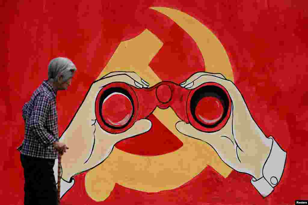 A woman stands near a mural showing an emblem of the Communist Party of China along a street in Shanghai, China.