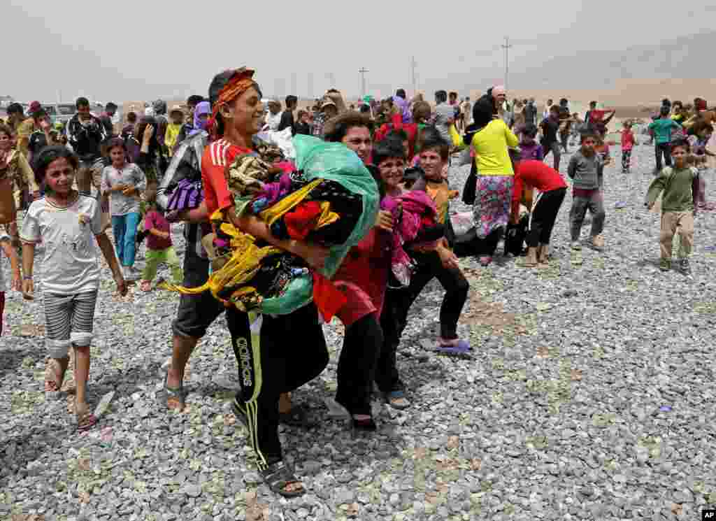 Displaced Iraqis carry clothes provided by a charity at a refugee camp, in Feeshkhabour town, Iraq, Aug. 19, 2014. 