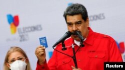 Le président vénézuélien Nicolas Maduro tenant un exemplaire miniature de la constitution lors d'une allocution en présence de son épouse Cilia Flores, après avoir voté aux élections régionales, à Caracas, le 21 novembre 2021.