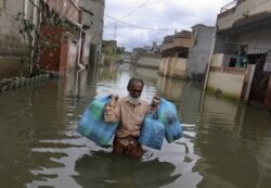 Seorang pria membawa barang saat mengarungi jalanan yang terdampak banjir akibat hujan lebat, di Karachi, Pakistan, Rabu, 26 Agustus 2020.