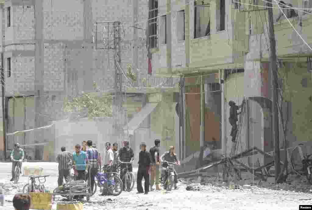 People stand past rubble of damaged buildings after what activists said was shelling by forces loyal to Syria's President Bashar al-Assad in Arbeen, outside Damascus, June 25, 2014. 