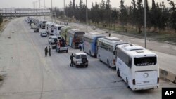 This photo released March, 22, 2018, by the Syrian official news agency SANA, shows Syrian government forces overseeing the evacuation by buses of rebel fighters and their families, at a checkpoint in eastern Ghouta, Syria.