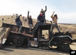 FILE - Protesters against the Dakota Access oil pipeline stand on a burned-out truck near Cannon Ball, N.D., that they removed from a long-closed bridge near their camp in North Dakota, Nov. 21, 2016.