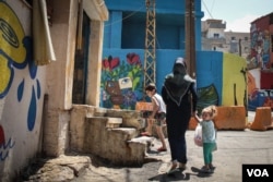 Residents walk past brightly painted walls in the Ouzai neighborhood. (J. Owens for VOA)