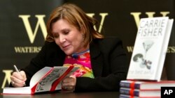 FILE - In this Feb. 20, 2004, photo, "Star Wars" actress, humorist and author Carrie Fisher autographs her book "The Best Awful" at a promotional event in London.