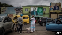 A woman sells beverages in front of electoral posters in Kinshasa, Democratic Republic of the Congo, Dec. 17, 2018.