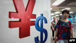 A woman walks past a yuan (L) and a US dollar (R) currency sign in Hong Kong on August 13, 2015.