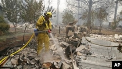 A firefighter with the Montezuma Fire District puts out hot spots at a home destroyed by fire Sunday, Sept. 13, 2015, in Middletown, California.