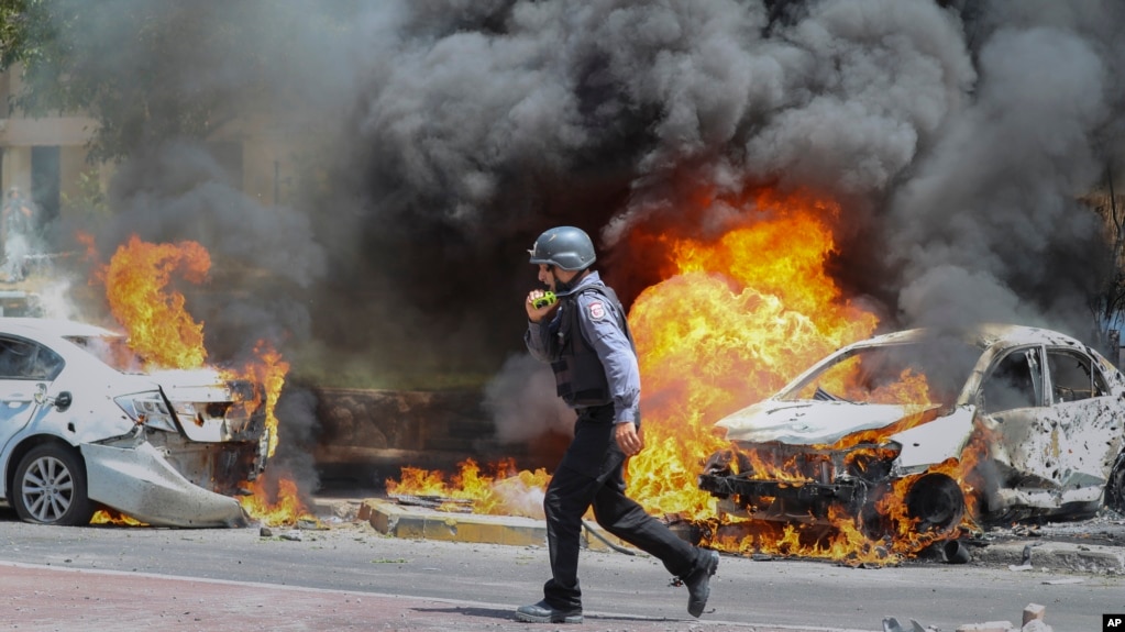 Seorang petugas pemadam kebakaran Israel berjalan di samping mobil yang terkena rudal yang ditembakkan dari Jalur Gaza, di kota Ashkelon di Israel selatan, Selasa, 11 Mei 2021. (AP Photo / Ariel Schalit)