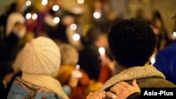 FILE - Community members place hands on each others shoulders during a candlelit vigil in support of the “safe harbor” legislation for child victims of human trafficking, Dec. 11, 2014, in Atlanta. 