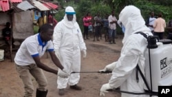 Health workers wash their hands after taking a blood specimen from a child to test for the Ebola virus in an area where a 17-year- old boy died from the virus on the outskirts of Monrovia, Liberia, June 30, 2015.