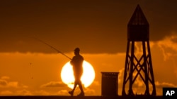 FILE - A fisherman prepares to cast a line as the sun rises behind him as he fishes off a jetty into the Atlantic Ocean, in Bal Harbour, Florida, July 14, 2016.