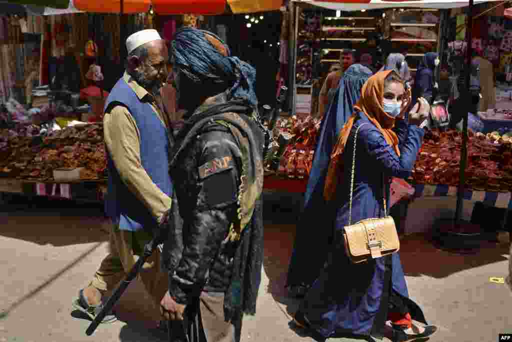 A Taliban fighter (C) walks past shoppers along Mandawi market in Kabul, Afghanistan, a day after the U.S. pulled all its troops out of the country to end a brutal 20-year war.